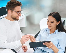 Man wearing white handing pen and clipboard to patient in dental chair
