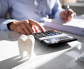 Someone at a desk with invoices, calculator, keyboard, and large model tooth casting a shadow on the white surface