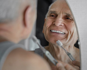 Man smiling and brushing his teeth in mirror