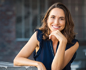 A middle-aged woman sitting a table and smiling after receiving her dental crowns in Downtown 