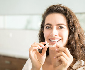 woman smiling while holding clear aligners