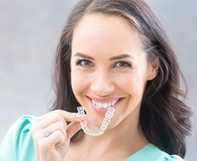 A young woman with dark hair preparing to insert her Invisalign aligner into her mouth while smiling
