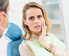 Woman in dental chair holding cheek in pain
