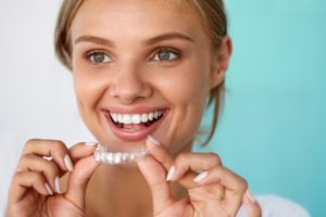 A woman smiling and holding a clear aligner.