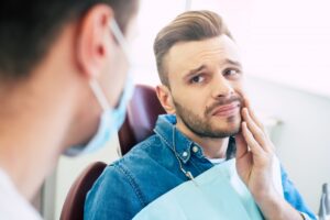 Young man holding mouth in pain in the dentist's chair.